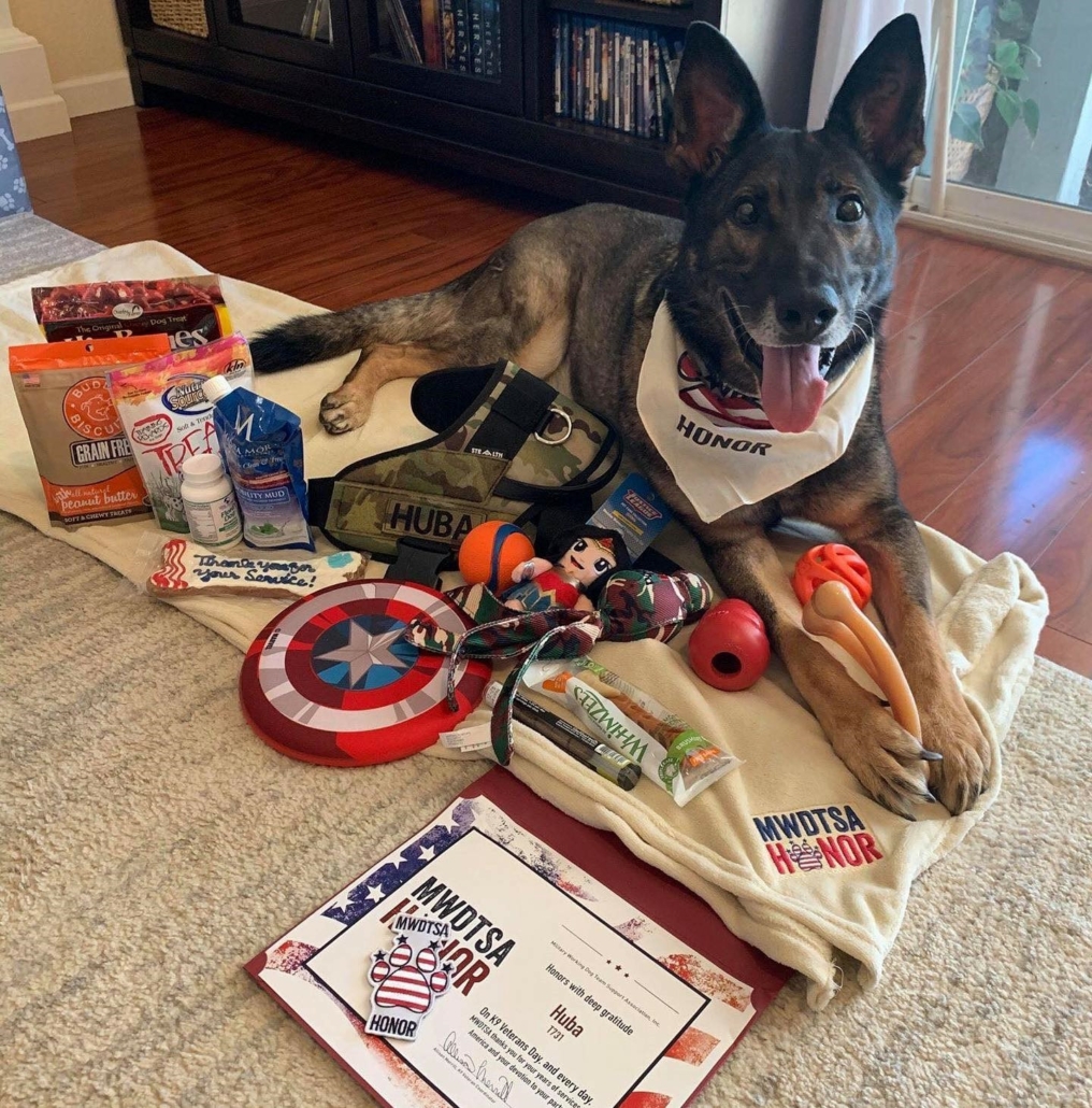 In this photo, RMWD Huba appears to be smiling while laying amidst the Honor Box goodies, which include dog treats, toys, a custom tactical vest, a blanket, a personalized certificate and more.