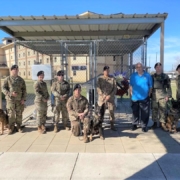 This photo shows handlers and their dogs, along with Security Forces Museum Director Ken Neal, standing in front of Nemo's Memorial at Lackland Air Force Base. In the background is a wreath donated by MWDTSA in honor of Vietnam veteran dog handler Bob Throneburg.